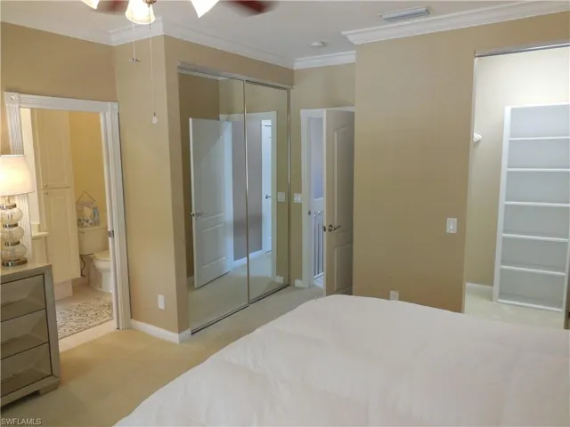 Bedroom featuring crown molding, light carpet, ensuite bath, a closet, and a ceiling fan