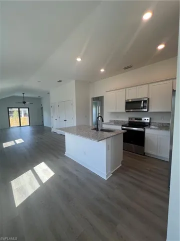 Kitchen with sink, a center island with sink, stove, light stone countertops, and white cabinets