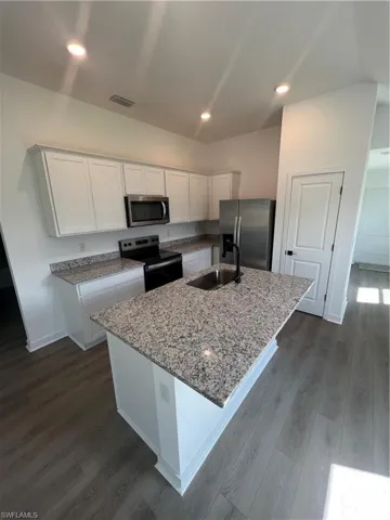 Kitchen with sink, white cabinetry, range, fridge, and an island with sink