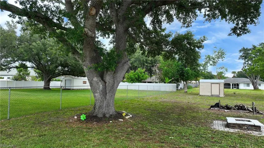 Expansive backyard featuring mature trees, a chain-link fence, a white vinyl privacy fence, a storage shed, and a built-in stone fire pit