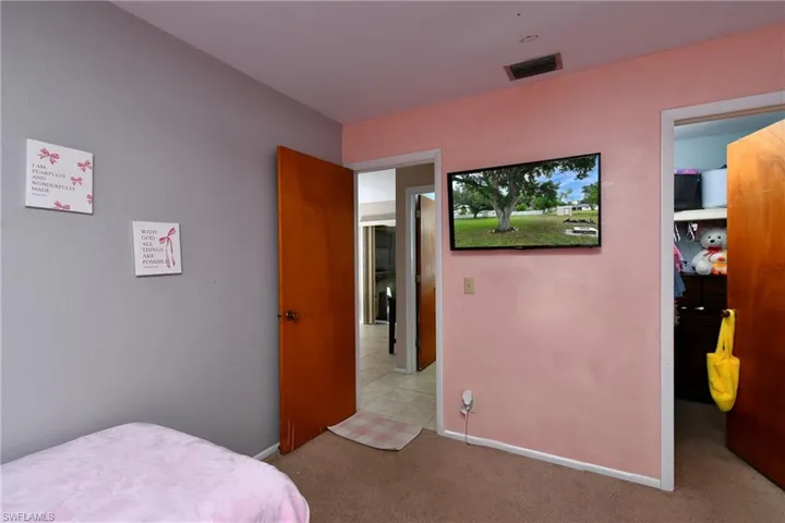 Carpeted room featuring a wall-mounted television, a built-in closet with shelving, and wood-finish doors