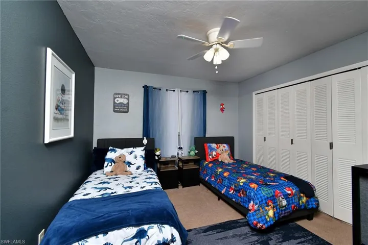 Bedroom featuring a ceiling fan with integrated lighting, louvered closet doors, a two-tone wall treatment, and carpet flooring