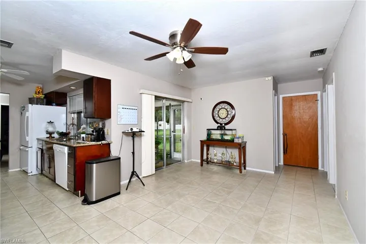 Open-concept living space featuring neutral tile flooring, a kitchen with dark wood-finish cabinetry, and a ceiling fan