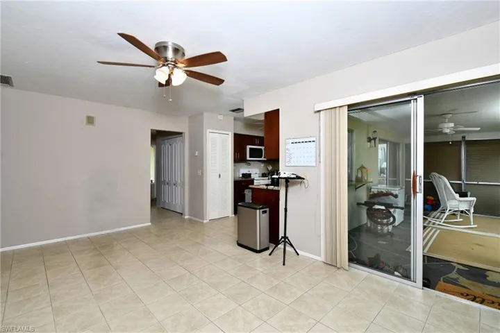 Spacious interior featuring neutral tone walls, large format tile flooring, a ceiling fan with integrated lighting, and sliding glass doors opening to an enclosed patio