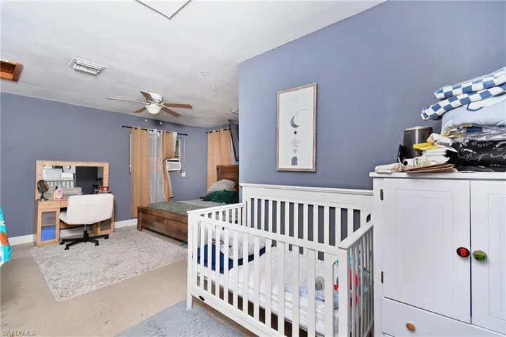 Converted Garage: Spacious interior featuring a ceiling fan, window-mounted air conditioning unit, and light-colored walls