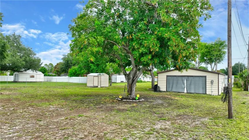 Expansive property featuring a mature shade tree, a detached metal garage with a roll-up door, and two additional storage sheds