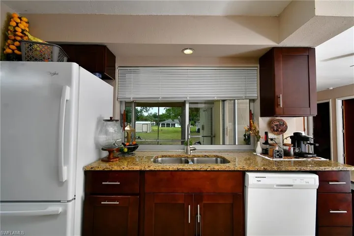 Kitchen featuring a double basin stainless steel sink, granite-style countertops, wood cabinetry, and a window with blinds