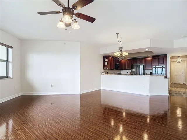 Unfurnished living room featuring dark hardwood / wood-style floors and ceiling fan with notable chandelier