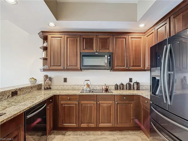 Kitchen with light stone countertops, kitchen peninsula, black electric cooktop, and refrigerator