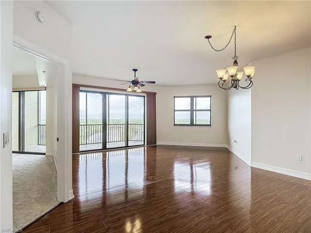 Empty room featuring dark hardwood / wood-style flooring and ceiling fan with notable chandelier
