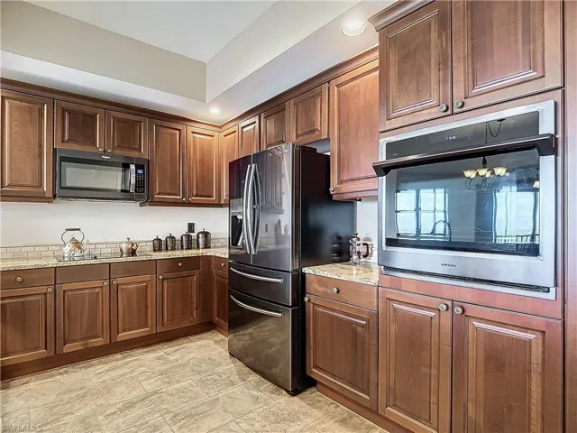 Kitchen with stainless steel oven, refrigerator with ice dispenser, light stone counters, and black electric cooktop