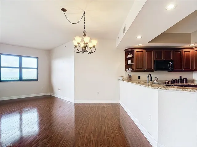 Kitchen featuring light stone countertops, dark hardwood / wood-style flooring, pendant lighting, and a notable chandelier