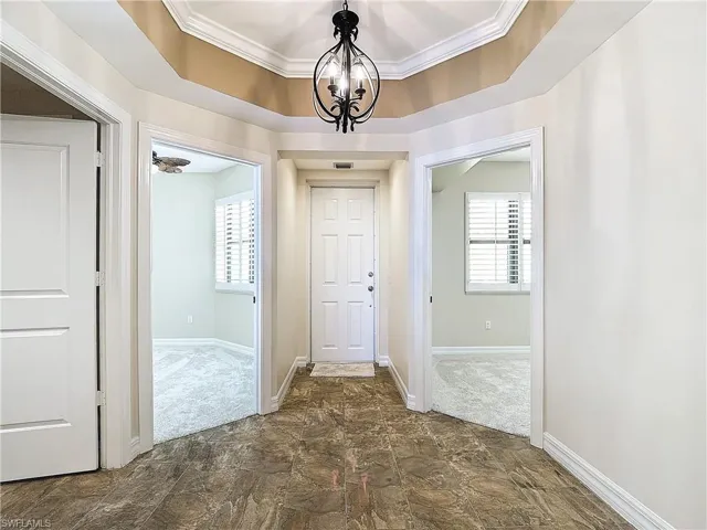 Corridor with dark colored carpet, ornamental molding, plenty of natural light, and a notable chandelier