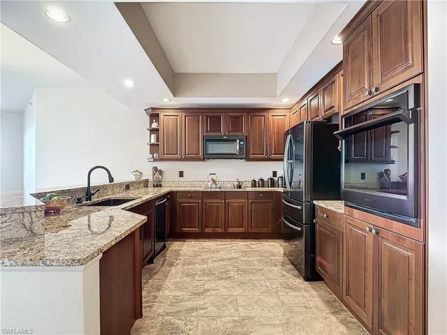 Kitchen with kitchen peninsula, sink, stainless steel refrigerator, black dishwasher, and light stone countertops