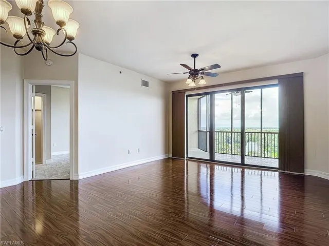 Spare room with dark hardwood / wood-style floors and ceiling fan with notable chandelier