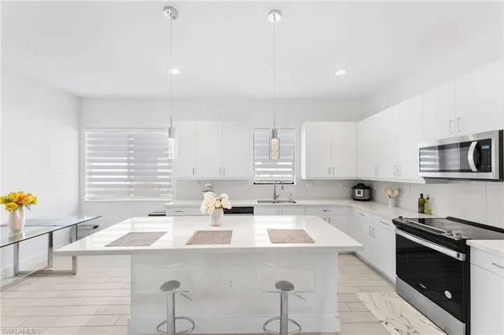 Kitchen featuring white cabinets, sink, decorative light fixtures, a kitchen bar, and stainless steel appliances