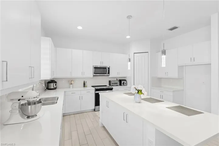 Kitchen featuring white cabinets, appliances with stainless steel finishes, and hanging light fixtures