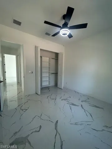 Unfurnished bedroom featuring light marble finish flooring, ceiling fan, and a closet