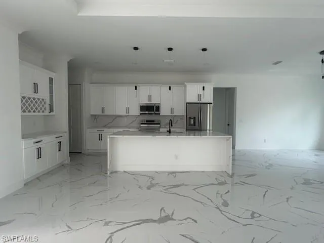Kitchen with a center island with sink, light stone counters, white cabinets, appliances with stainless steel finishes, and light marble finish floors