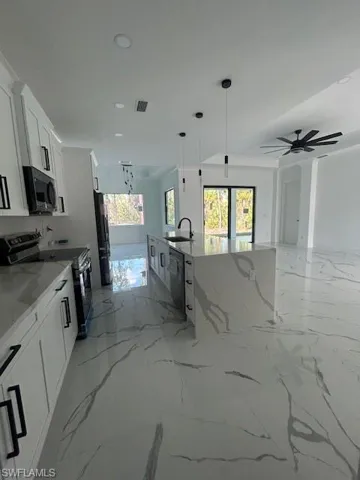 Kitchen with light marble finish flooring, stove, light stone counters, hanging light fixtures, and recessed lighting
