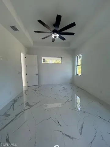 Spare room featuring light marble finish floors, a raised ceiling, and healthy amount of natural light