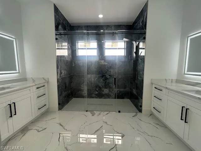 Bathroom with two vanities, a marble finish shower, and light marble finish floors