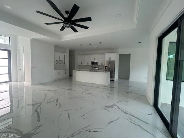 Unfurnished living room with light marble finish flooring, a raised ceiling, ceiling fan, and recessed lighting