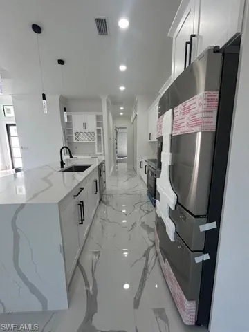 Kitchen with white cabinetry, open shelves, recessed lighting, light marble finish flooring, and fridge