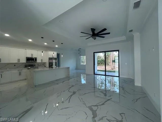 Living room featuring a raised ceiling, light marble finish floors, recessed lighting, and a ceiling fan