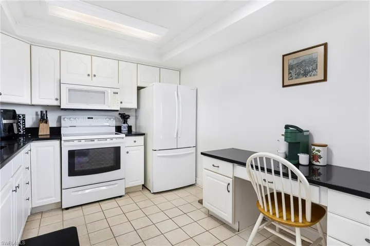 Kitchen featuring light tile patterned floors, white cabinetry, white appliances, and a raised ceiling