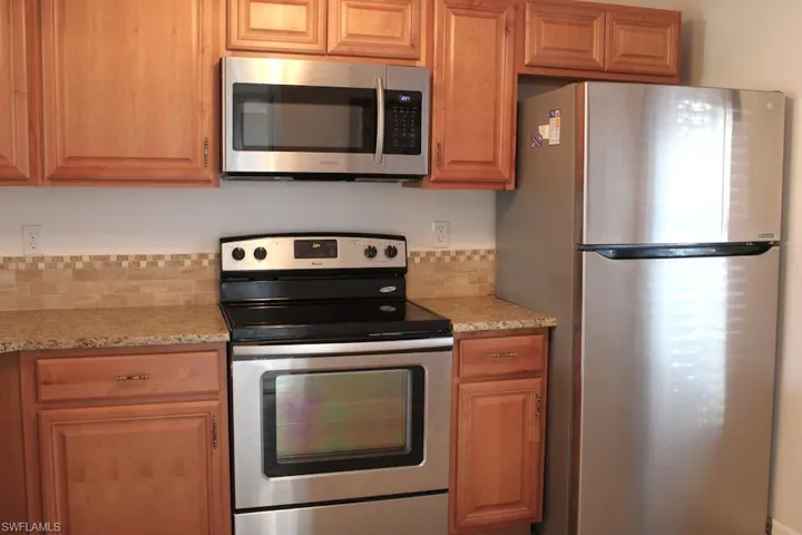 Kitchen with appliances with stainless steel finishes, light stone countertops, and brown cabinets