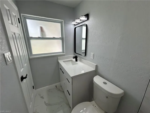 Bathroom with vanity, marble look tile flooring, toilet, and baseboards