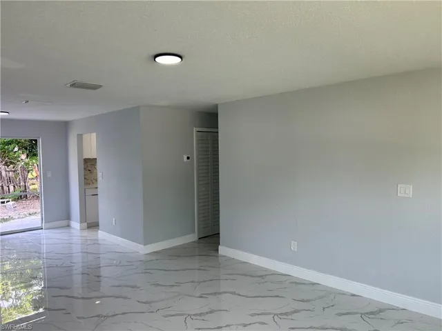 Spare room featuring light marble finish floors, baseboards, and a textured ceiling