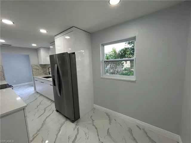 Kitchen featuring stainless steel fridge with ice dispenser, light marble finish floors, white cabinets, baseboards, and recessed lighting