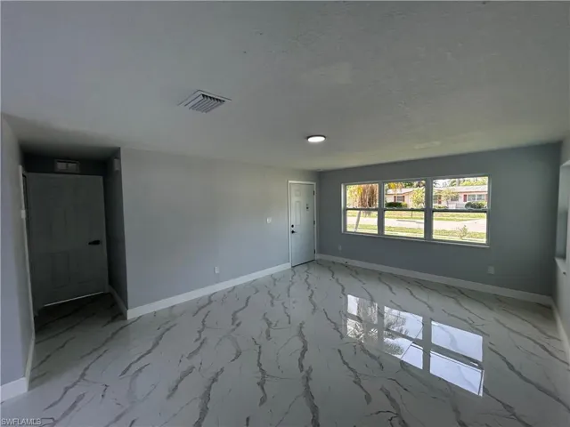 Empty room featuring marble finish flooring, baseboards, and a textured ceiling