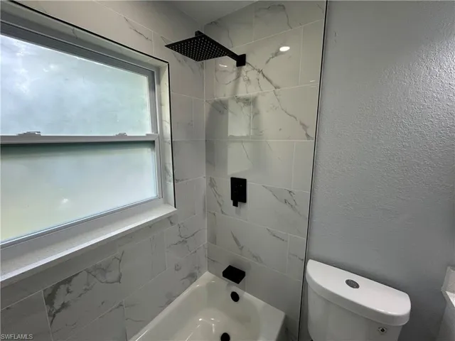 Bathroom featuring toilet, shower / bath combination, and a textured wall