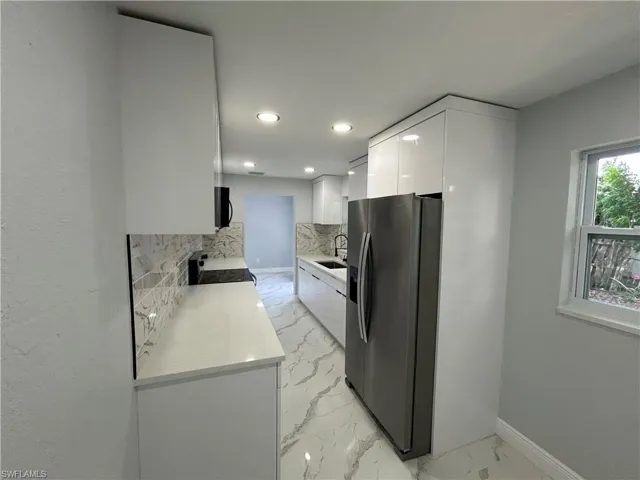 Kitchen with stainless steel refrigerator with ice dispenser, stove, modern cabinets, white cabinetry, and light marble finish flooring