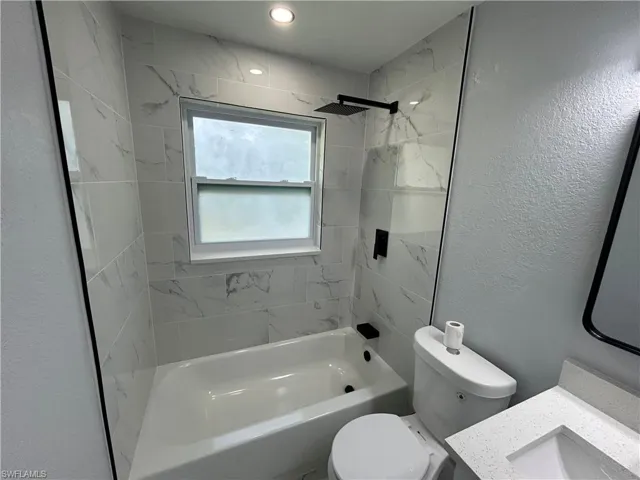 Full bath featuring shower / washtub combination, toilet, vanity, and a textured wall