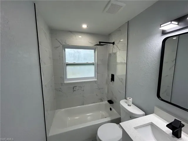 Bathroom with shower / bathtub combination, toilet, vanity, and a textured wall