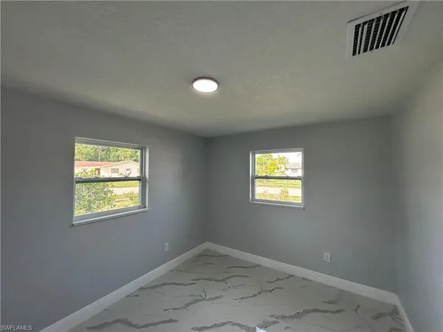 Spare room featuring light marble finish floors, healthy amount of natural light, baseboards, and a textured ceiling