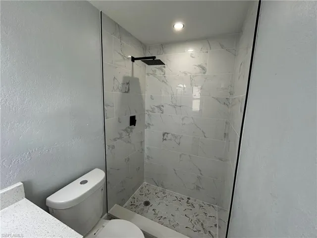 Bathroom with tiled shower, toilet, vanity, and recessed lighting