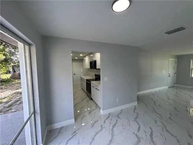 Kitchen featuring electric range, baseboards, black microwave, and white cabinetry