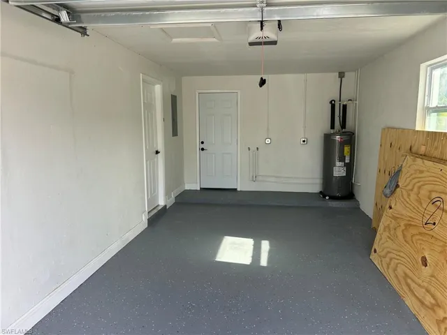 Garage with electric water heater, a garage door opener, electric panel, and baseboards