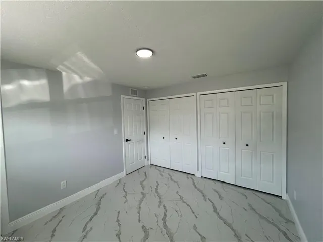 Unfurnished bedroom with baseboards, multiple closets, and marble look tiles
