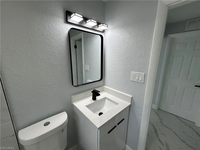 Half bath with vanity, toilet, marble look tile flooring, and a textured wall