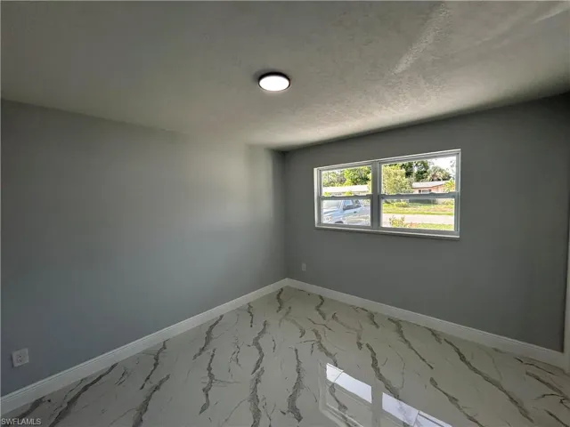 Spare room featuring light marble finish floors, baseboards, and a textured ceiling