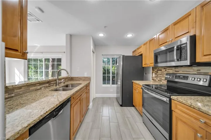 Kitchen with backsplash, appliances with stainless steel finishes, light stone countertops, recessed lighting, and wood finish floors