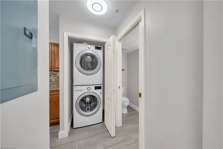 Laundry room with electric panel, stacked washer / drying machine, and wood finish floors