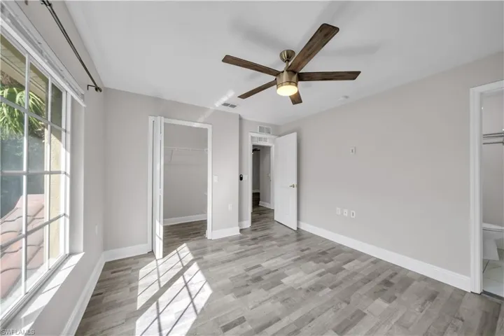 Unfurnished bedroom featuring ensuite bath, light wood-style floors, a walk in closet, and a ceiling fan
