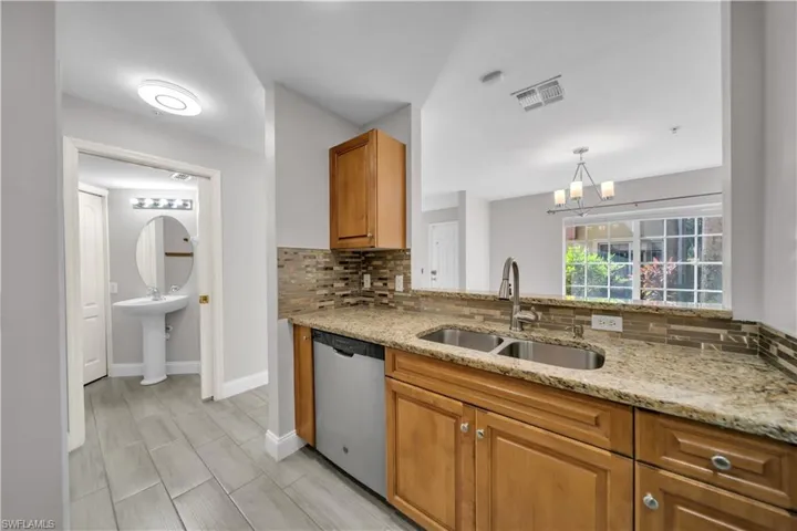 Kitchen featuring decorative backsplash, light stone countertops, dishwasher, a chandelier, and decorative light fixtures